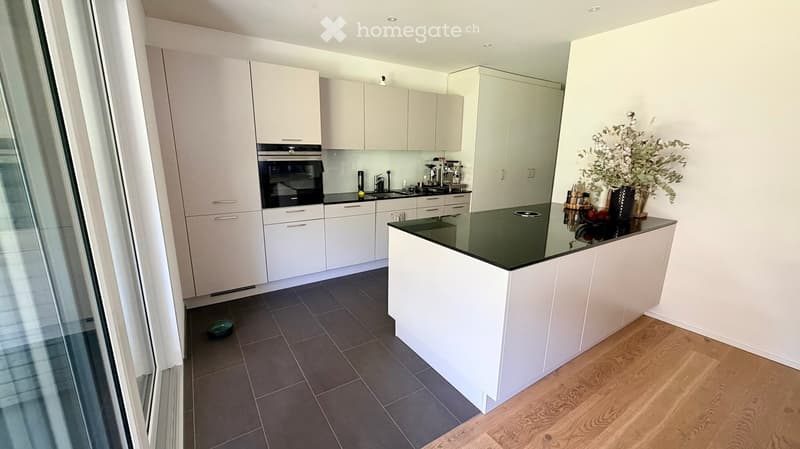 Modern kitchen with white cabinets, black countertop, built-in oven, and various appliances. Includes a vase with flowers on the island.