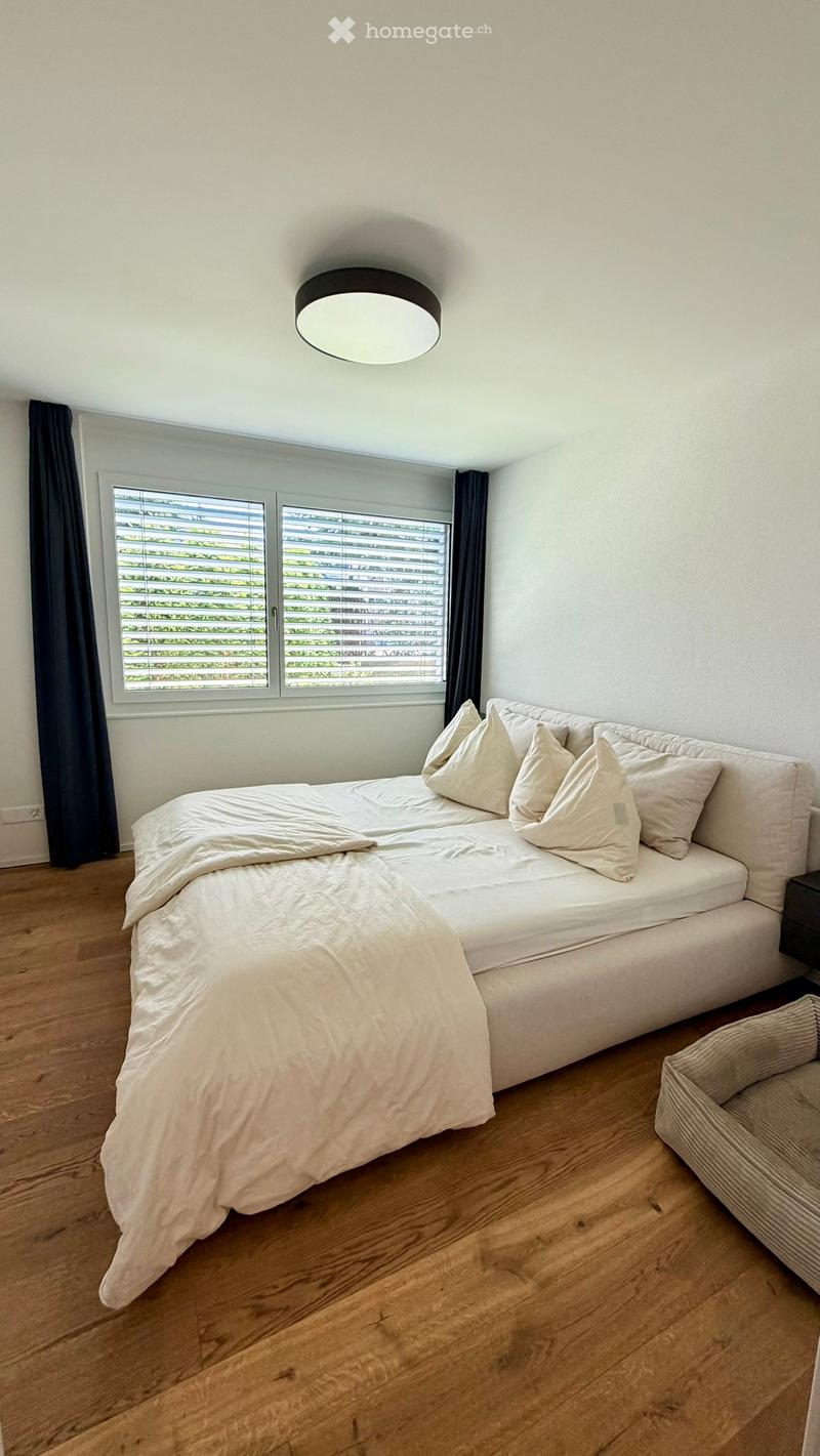 Modern bedroom with a large window, wooden floor, a sofa bed with pillows and a blanket, and a nightstand.