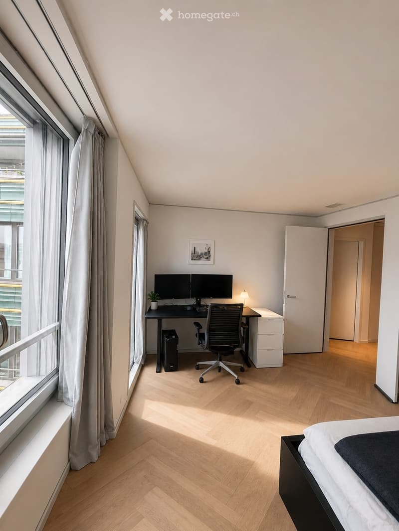 Modern, well-lit room with a bed, desk, and office chair. Features large windows with curtains, wooden flooring, and a small plant on the desk.