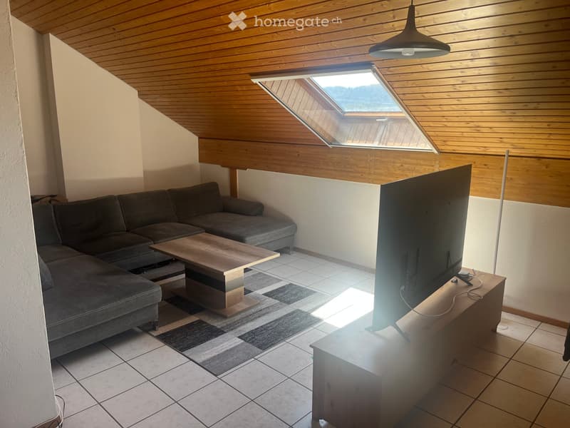 Modern living room with a grey sectional sofa, wooden coffee table, flat-screen TV on a wooden stand, and a skylight window above.