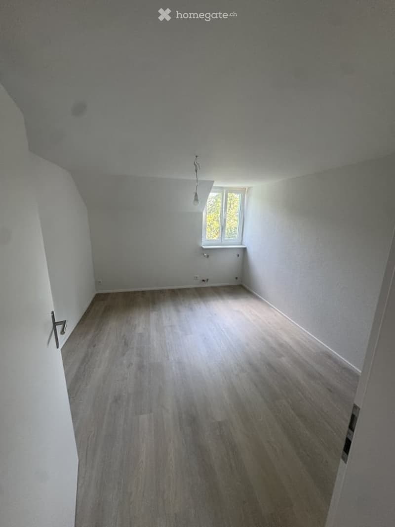 Empty room with light wooden flooring, white walls, and a single window letting in natural light. No furniture or equipment present.