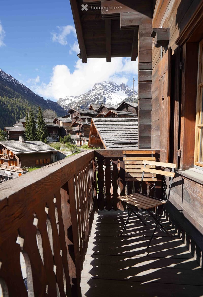 Balcony with wooden railing and a view of snow-capped mountains and village houses.