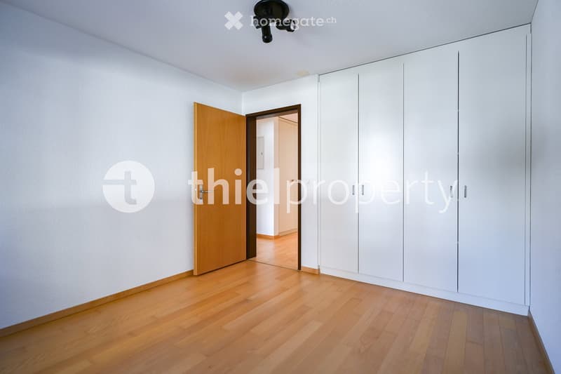 Empty room with light wooden flooring, white walls, built-in white wardrobes, and an open doorway leading to another room.