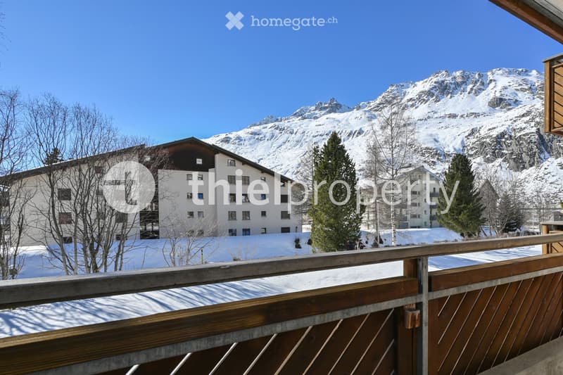 Balcony overlooking a snow-covered landscape with a large building and snow-capped mountains in the background.