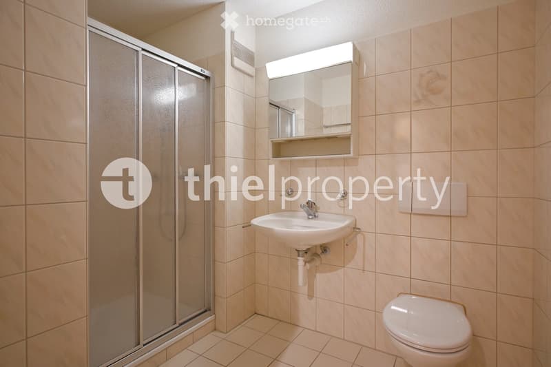 Modern bathroom with beige tiles, a white sink, a toilet, a mirror with built-in lighting, and a glass-enclosed shower stall.