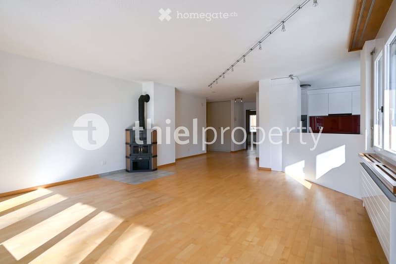 Bright, open living space with wooden flooring, a fireplace, and modern lighting fixtures. The room features large windows allowing natural light to fill the space.