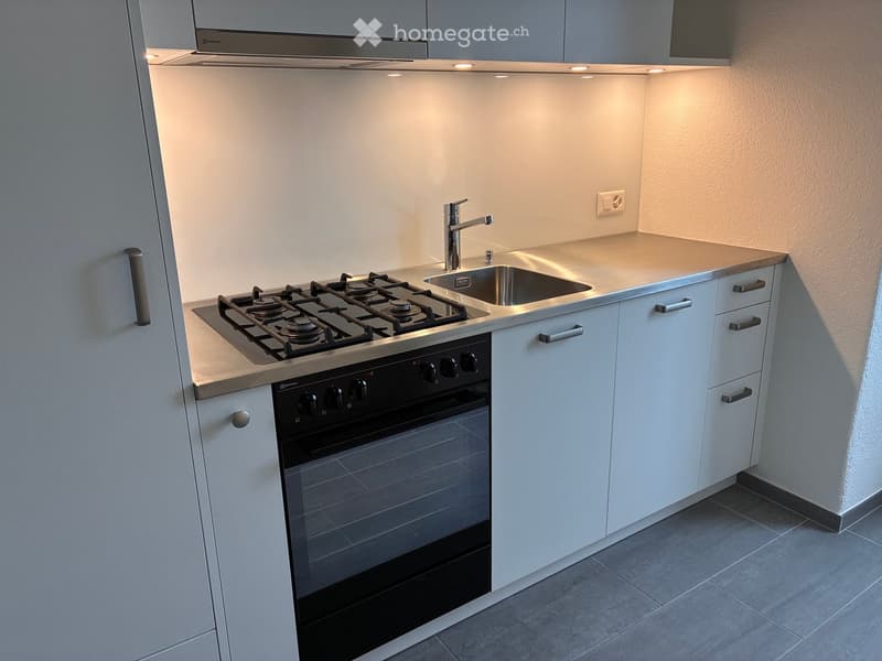 Modern kitchen with white cabinets, gas stove, oven, sink, and faucet.