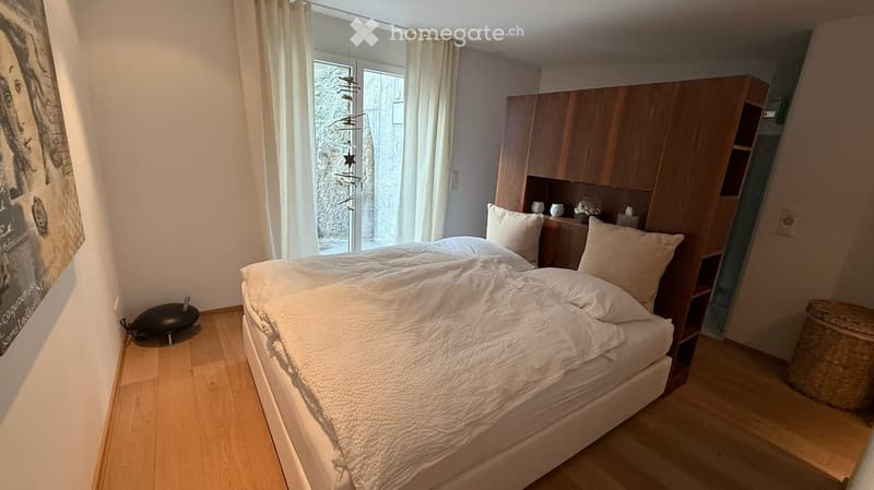 white bed, white comforter, 2 white pillows, wooden shelves, white curtains, large window
