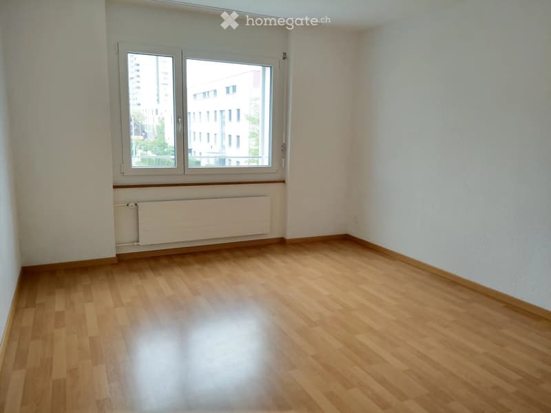 Empty room with wooden flooring, white walls, large windows, and a radiator under the windows.