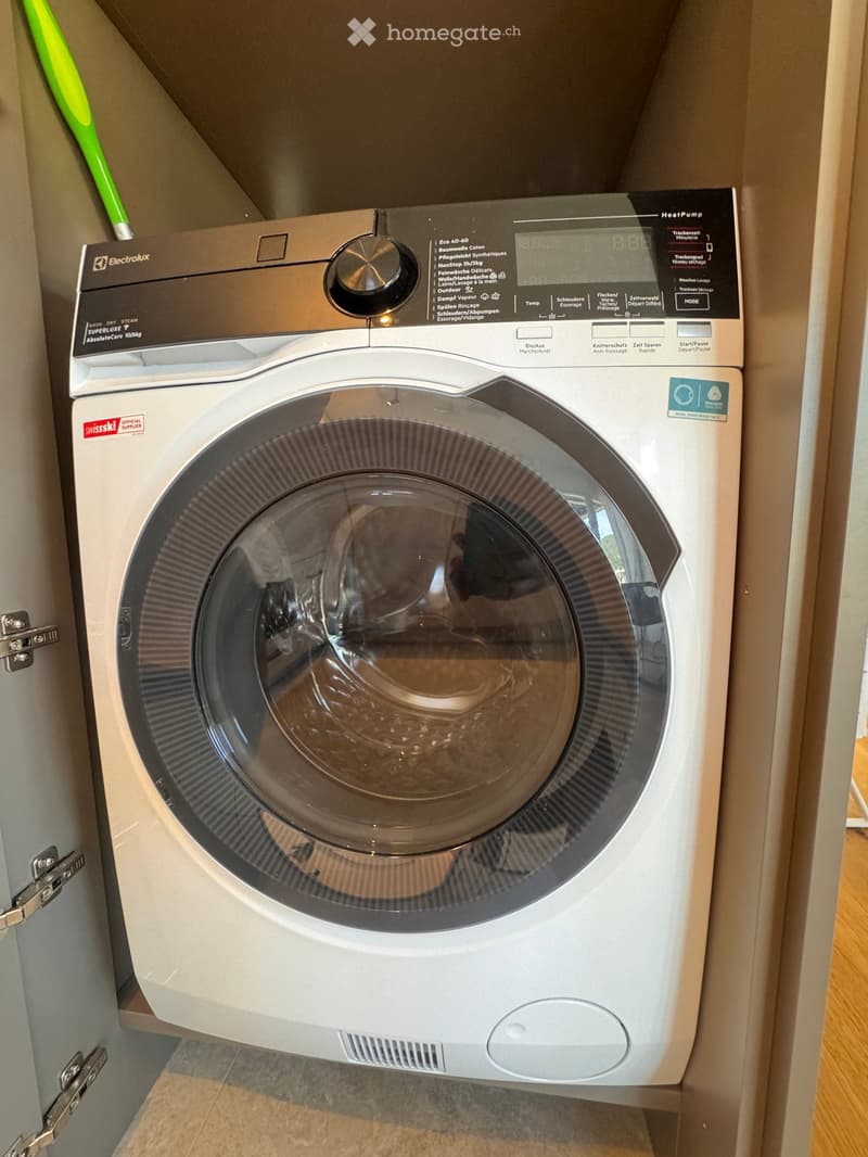 A modern washing machine with a digital control panel, placed in a tiled bathroom area.