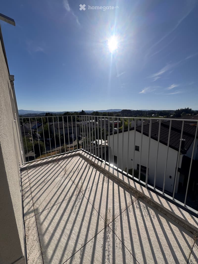 Balcony with metal railing, tiled floor, and scenic view of surrounding buildings and landscape.