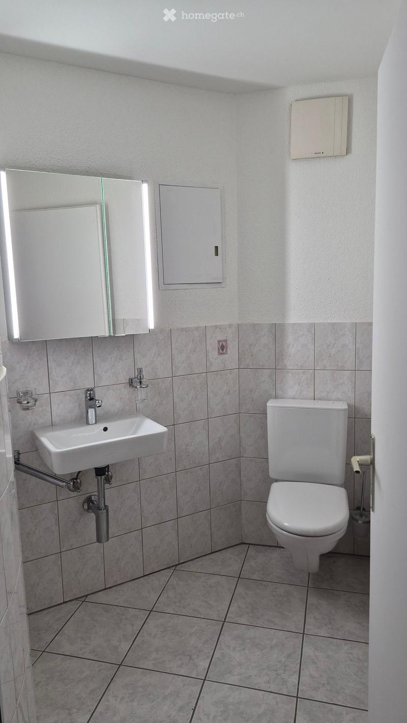 Modern bathroom with white tiles, a sink, a toilet, a mirror, and a cup on the sink.