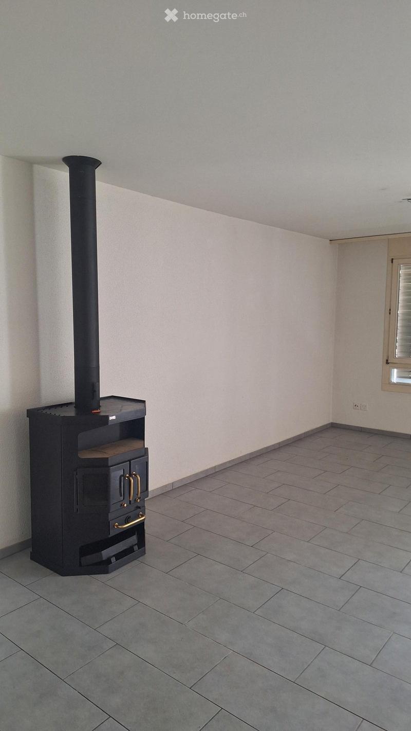Empty room with tiled floor, light-colored walls, and a black wood-burning stove with a chimney.