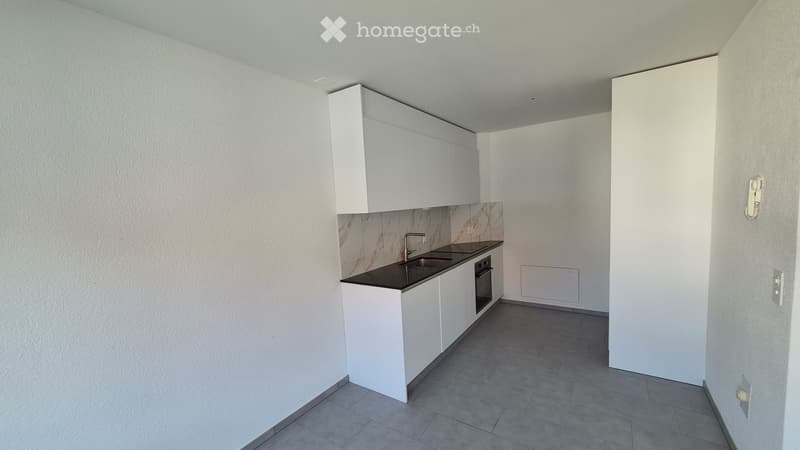 Modern kitchen with white cabinets, black countertop, sink, faucet, and built-in oven. Grey tiled floor and white walls.