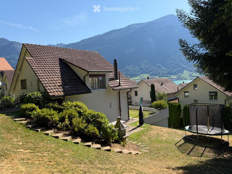 A well-maintained garden with a trampoline, surrounded by houses and a scenic mountain view.