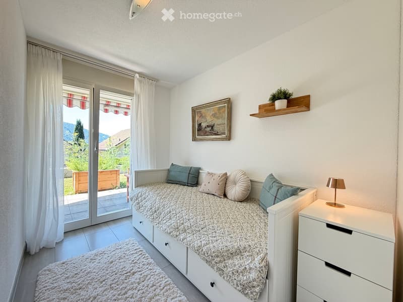 Cozy bedroom with a single bed, nightstand, lamp, picture frame, shelf with a potted plant, and a rug.