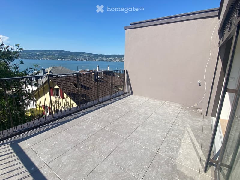 Balcony with tiled floor, metal railing, and scenic view of a lake and distant hills.