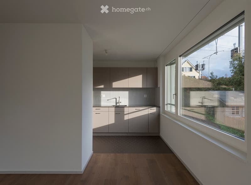 Empty kitchen with light-colored cabinets, a sink, and large windows overlooking a street.