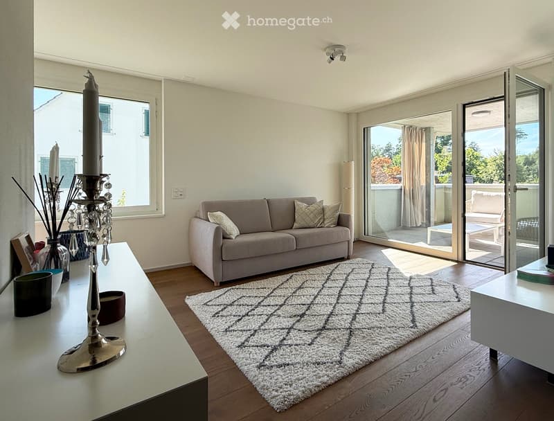 Modern living room with a grey sofa, coffee table, decorative candle holder, and a view to a balcony.