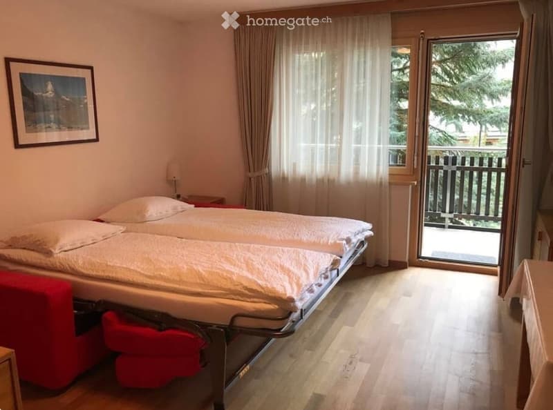 Cozy bedroom with a double bed, nightstand, lamp, and a large window with a view of the balcony.