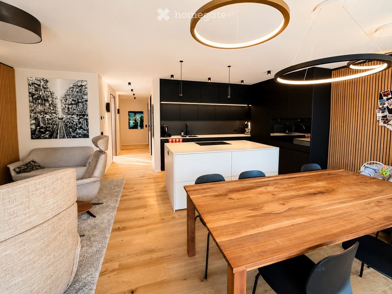 Open-plan living and dining area with a modern kitchen, wooden flooring, pendant lights, and contemporary furniture.