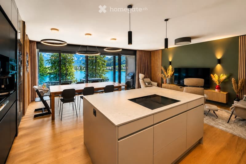 Modern open-plan living and dining area with a central kitchen island, dining table, and comfortable seating, featuring large windows with scenic mountain views.