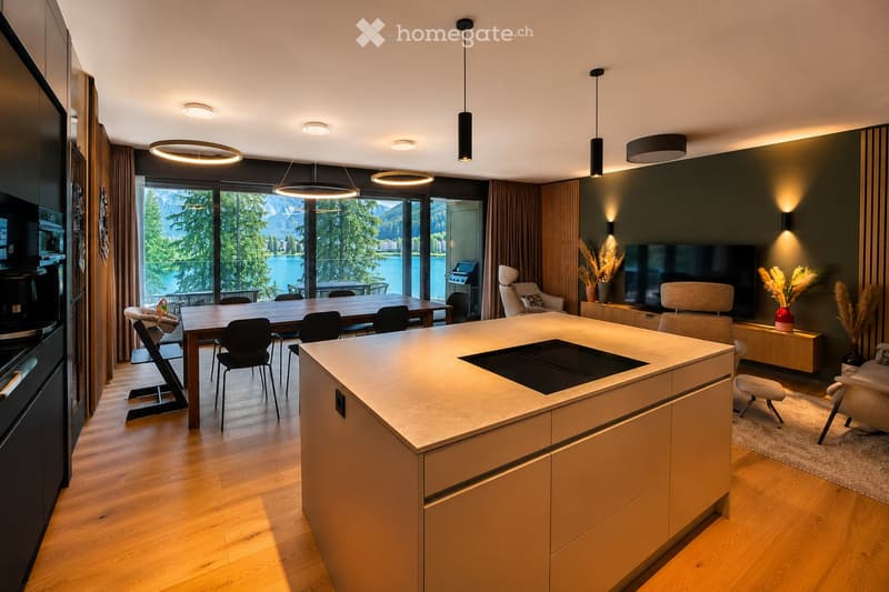 Modern kitchen and dining area with a central island, dining table, chairs, sofa, TV, and decorative vases.