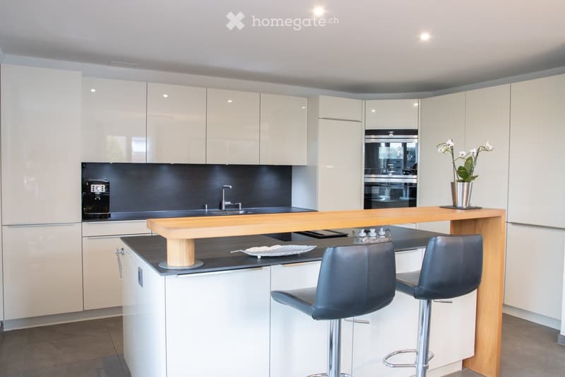 Modern kitchen with white cabinets, a wooden island, two bar stools, a coffee maker, and a vase with flowers on the island.