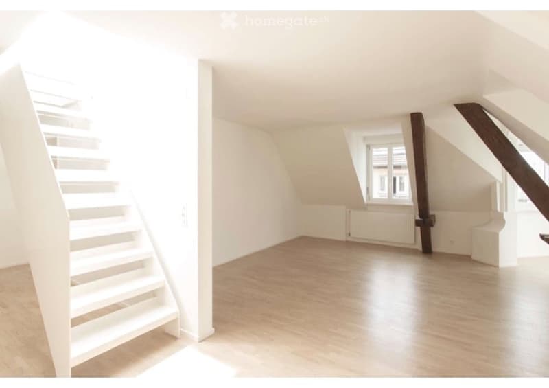 Completely empty room with wooden floor, white walls, and a staircase leading up. No furniture or equipment.