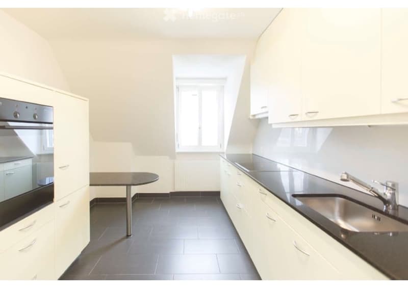 Modern kitchen with white cabinets, black countertops, stainless steel sink, and a small round table.