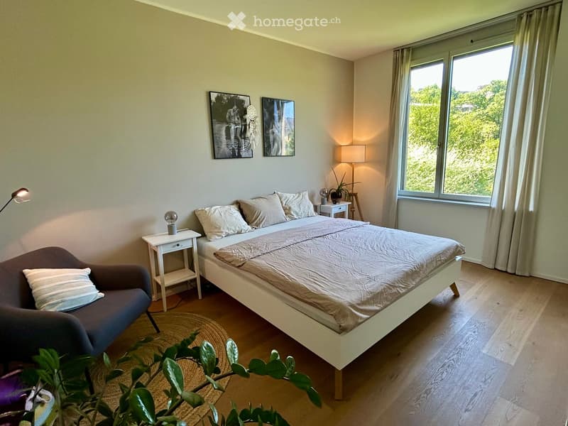 Modern bedroom with a large bed, nightstands, a sofa, wall art, and a plant near the window.