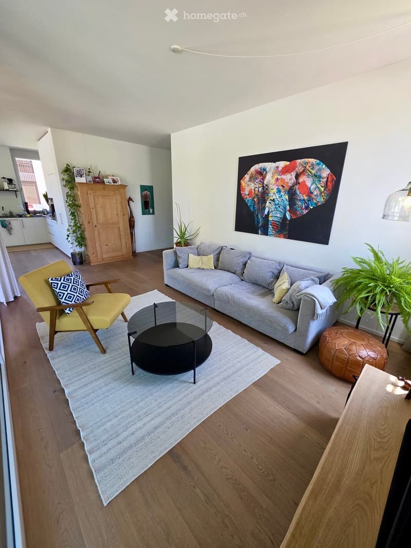 Modern living room with light wooden flooring, a grey sectional sofa, a yellow armchair, a black coffee table, and a large abstract painting on the wall.