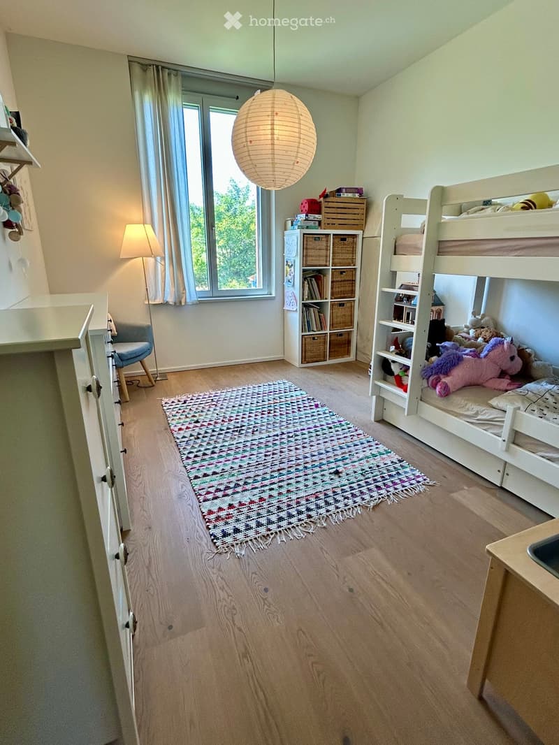 Bright, cozy bedroom with wooden flooring, bunk bed, colorful rug, and storage shelves.