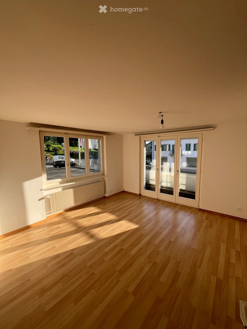 Empty room with wooden flooring, large windows, and sliding glass doors leading to a balcony.