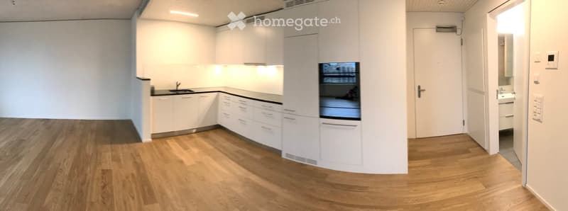 Open-plan kitchen and hallway area with white cabinetry, wooden flooring, and built-in appliances.