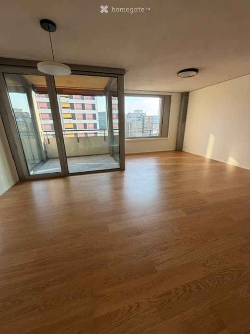 Empty room with wooden flooring, large glass sliding doors leading to a balcony, and white walls.