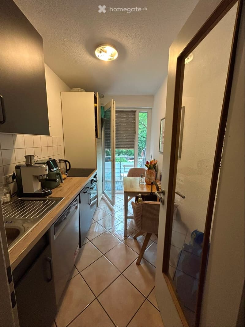 A compact kitchen with modern appliances, including a coffee maker, dishwasher, and oven. A small dining area with a table and chair is visible, leading to a balcony with outdoor seating.