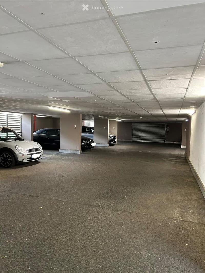 Underground parking area with several parked cars, numbered stalls, and a clean, organized space.