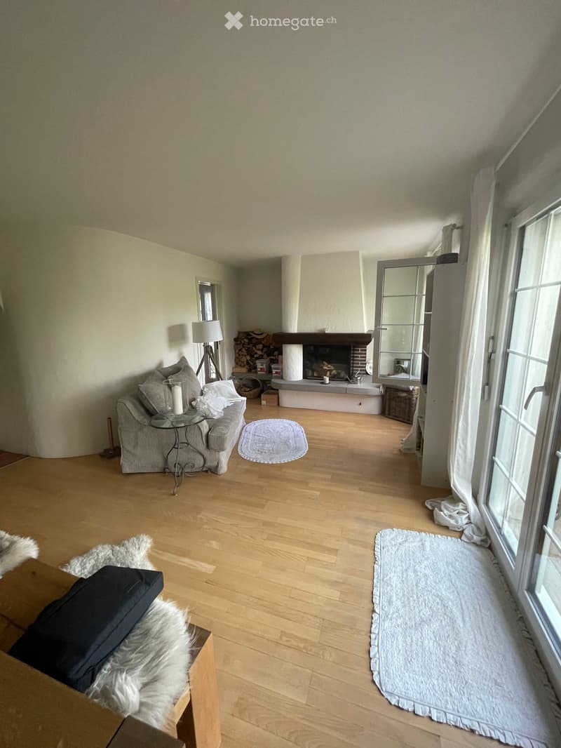Living room with light wooden flooring, fireplace, sofa, coffee table, floor lamp, and large windows.