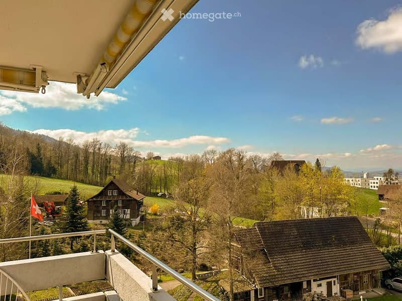 Balcony overlooking a scenic countryside with houses, trees, and a clear blue sky.
