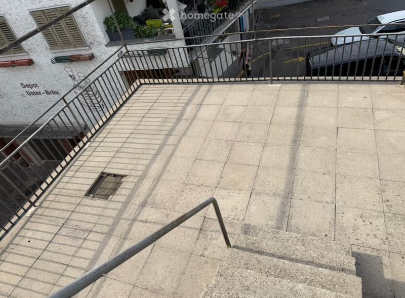 Balcony with tiled floor, metal railing, and steps leading up, with a view of a parked car and part of a building.