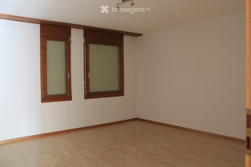 Empty room with wooden flooring, white walls, and two windows with wooden frames and blinds.