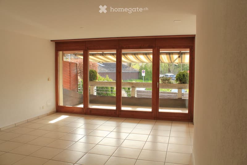 Empty room with tiled floor and large wooden sliding doors leading to a balcony area. The space is well-lit with natural light coming through the glass panels.