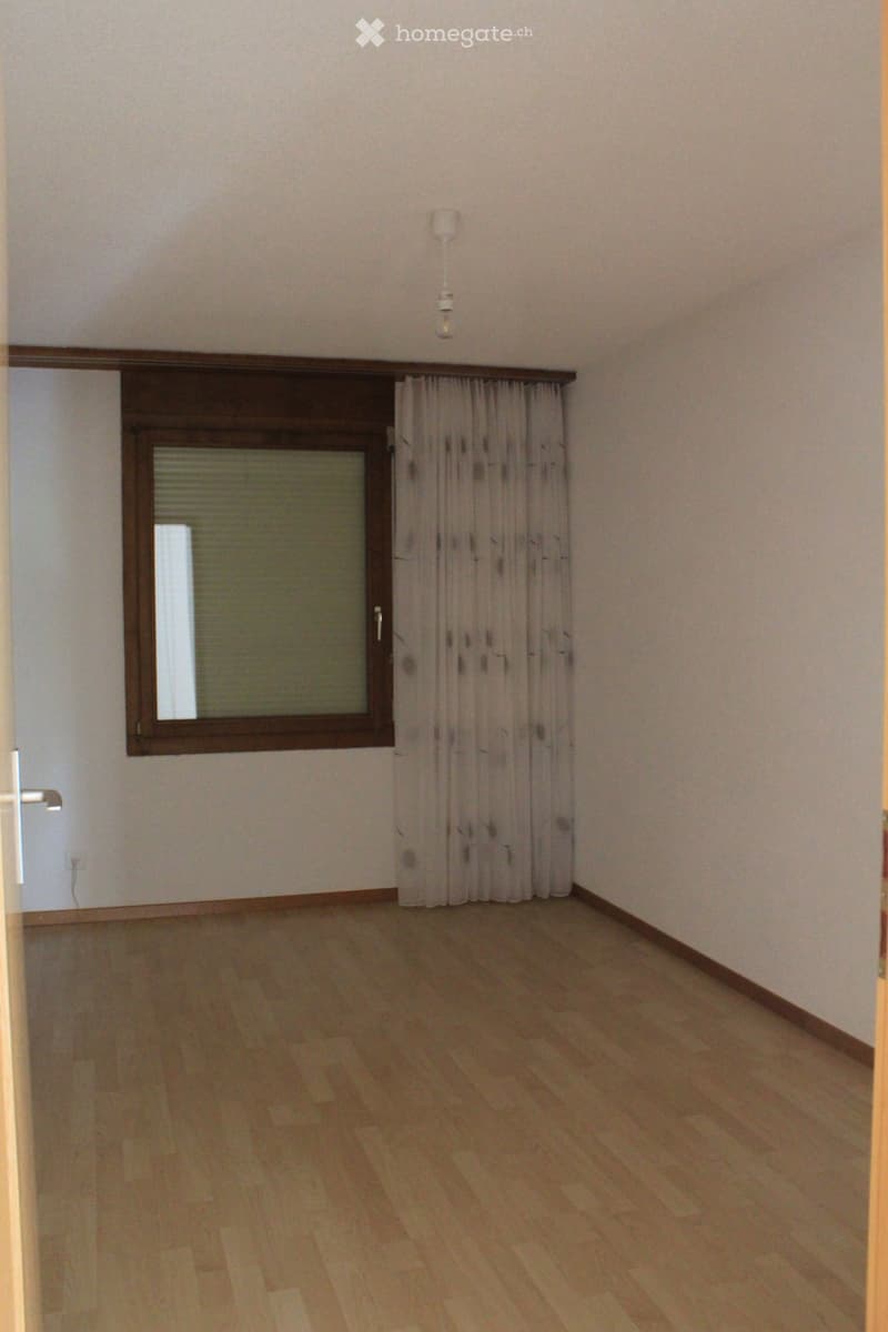 Empty room with wooden flooring, white walls, and a window with curtains. No furniture or equipment is present.