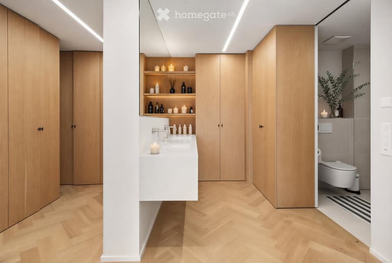 Modern bathroom with herringbone wooden flooring, white sink with chrome faucet, built-in wooden cabinets, shelves with candles and bottles, and a toilet in the adjacent space.