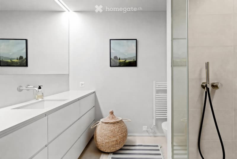 Modern bathroom with white cabinets, a sink, a shower with a glass enclosure, a towel rack, and a wicker basket on the floor.