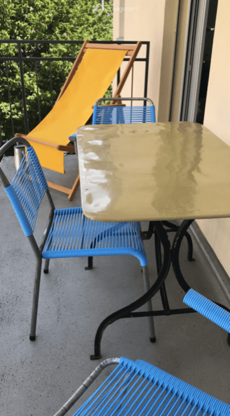 Balcony with a table and chairs, a lounge chair, and a view of greenery.