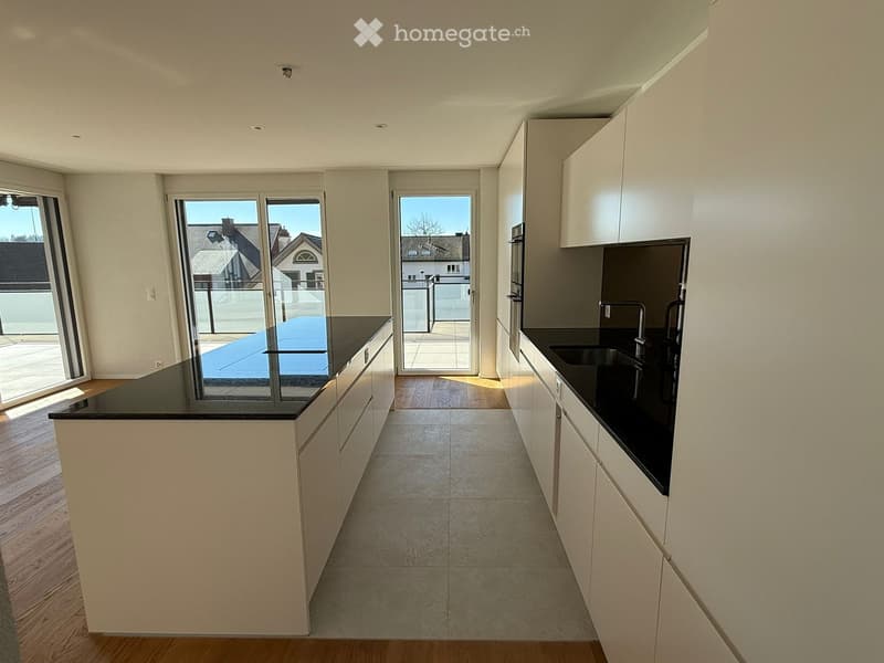 Modern kitchen with white cabinets, black countertops, and a central island. Large windows and sliding doors lead to a balcony.