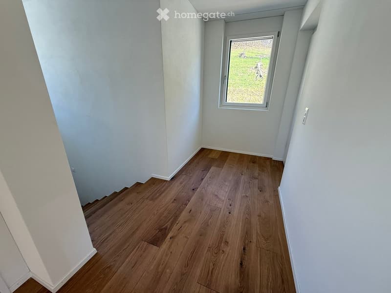 Empty room with light wooden flooring and white walls, featuring a single window with a view of a grassy area.