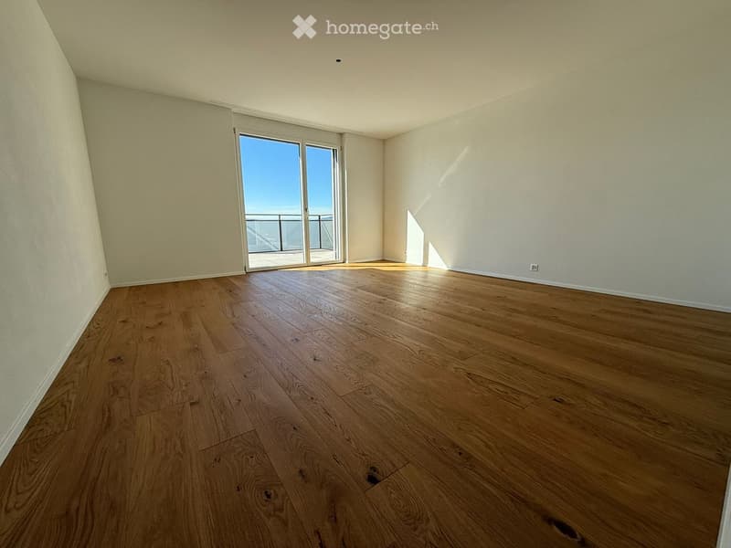 Empty room with wooden flooring, white walls, and a large sliding glass door leading to a balcony.